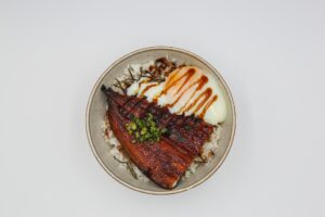 Unagi in a bowl of rice with an eel sauced egg on the side and scallions on top.