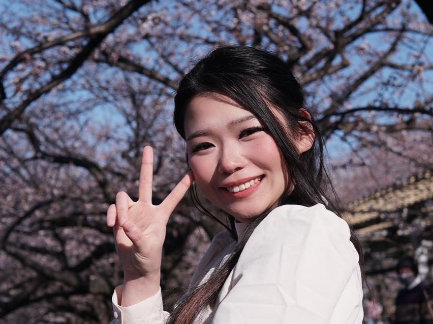 Hazunats smiling at the camera while showing a peace sign during a hanami.