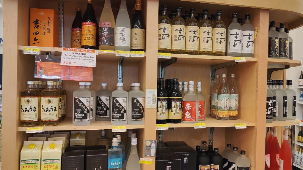 Wooden shelf filled with different types of shochu at a supermarket.