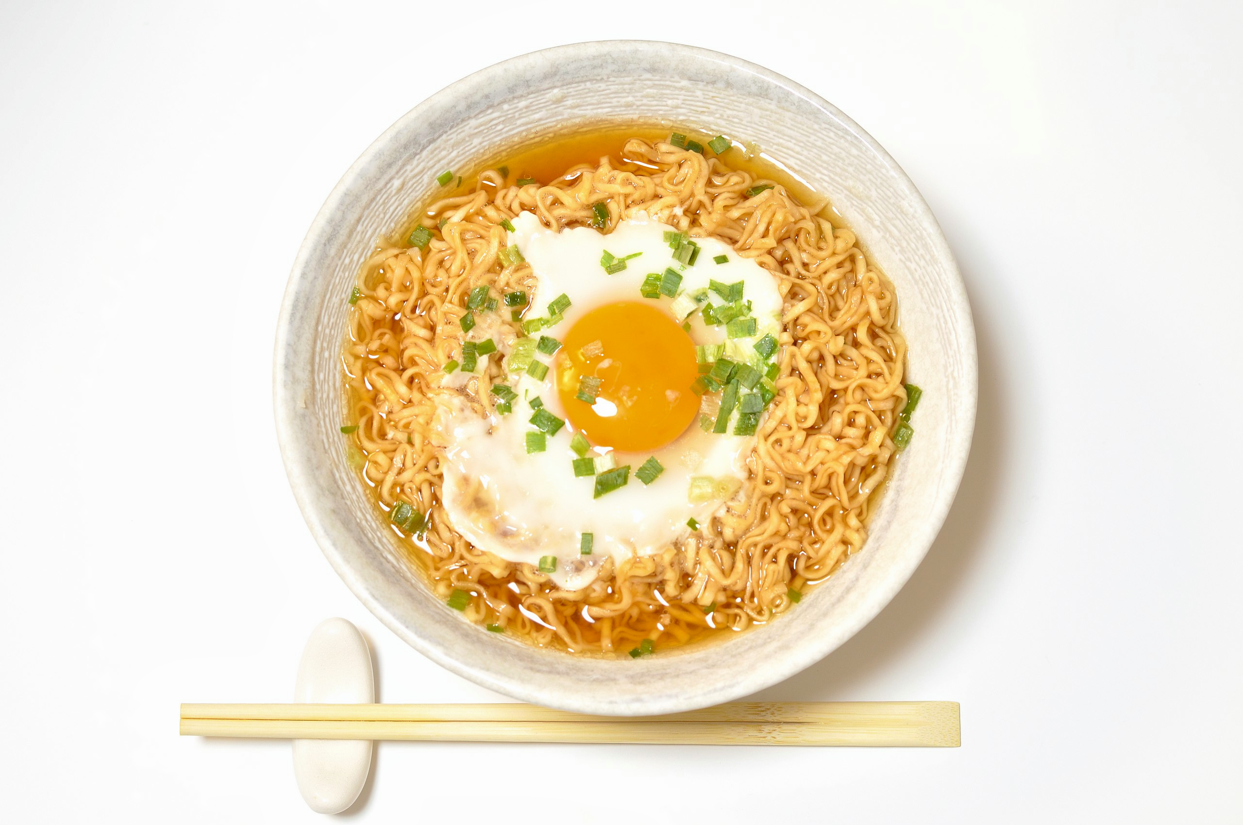 A bowl of the original Nissin Chikin ramen (which was invented by Momofuku Ando) with an egg on top and green onions sprinkled around.