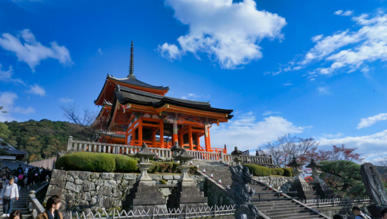 A view of the Kiyomizu-dera temple from the front-left side looking up towards the middle on a sunny day with clear skies.