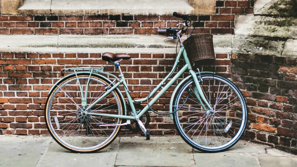 A mamachari bicycle with a wicker basket at the front leaning against a brick wall.