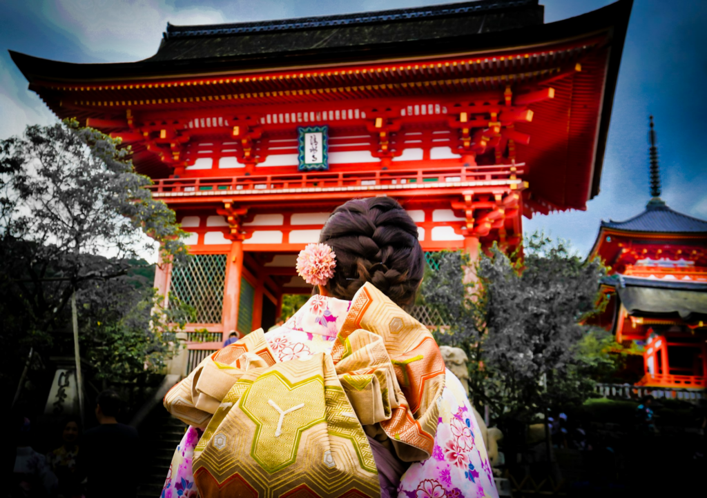 A woman with braided hair in a kimono walking towards the Nio-mon entrance of Kiyomizu-dera.